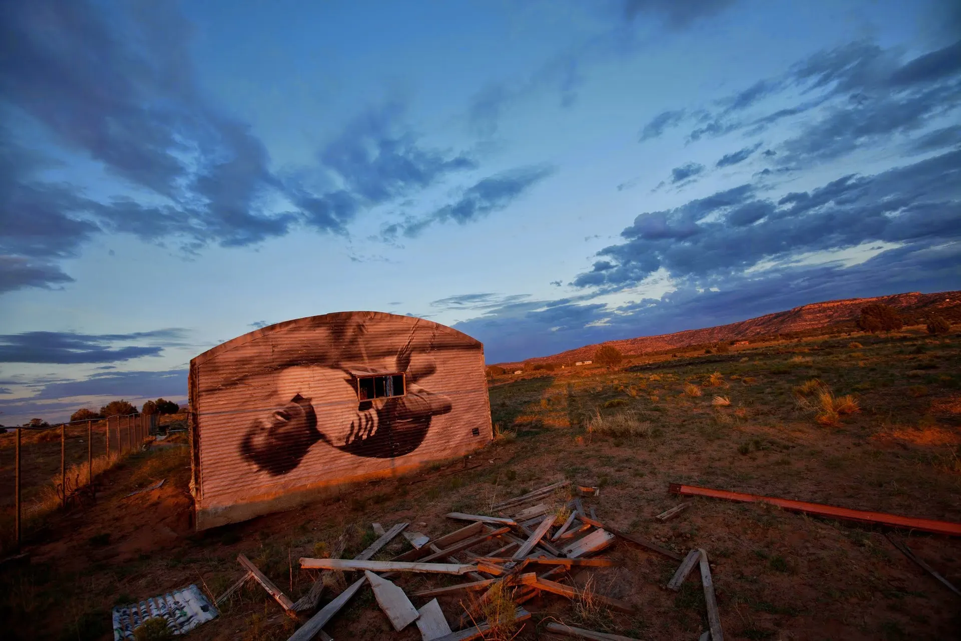 Photo of an isoalted building in a desert landscape with a large mural of black woman on a swing.