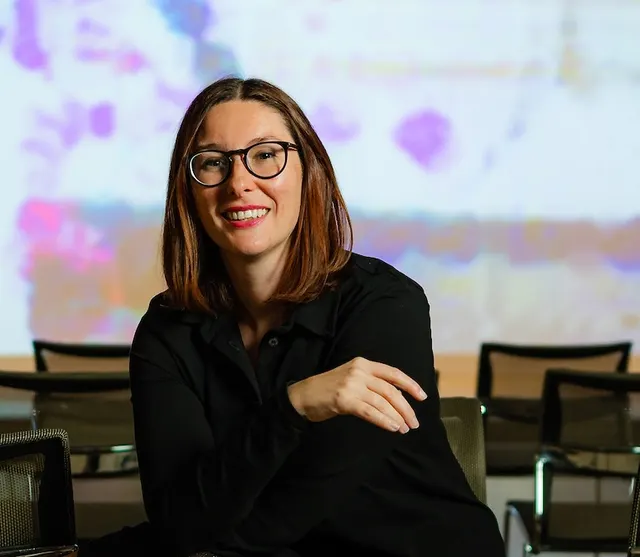 Photo portrait of Kate in color, white woman with dark hair and glasses, looking at the camera with a smile.