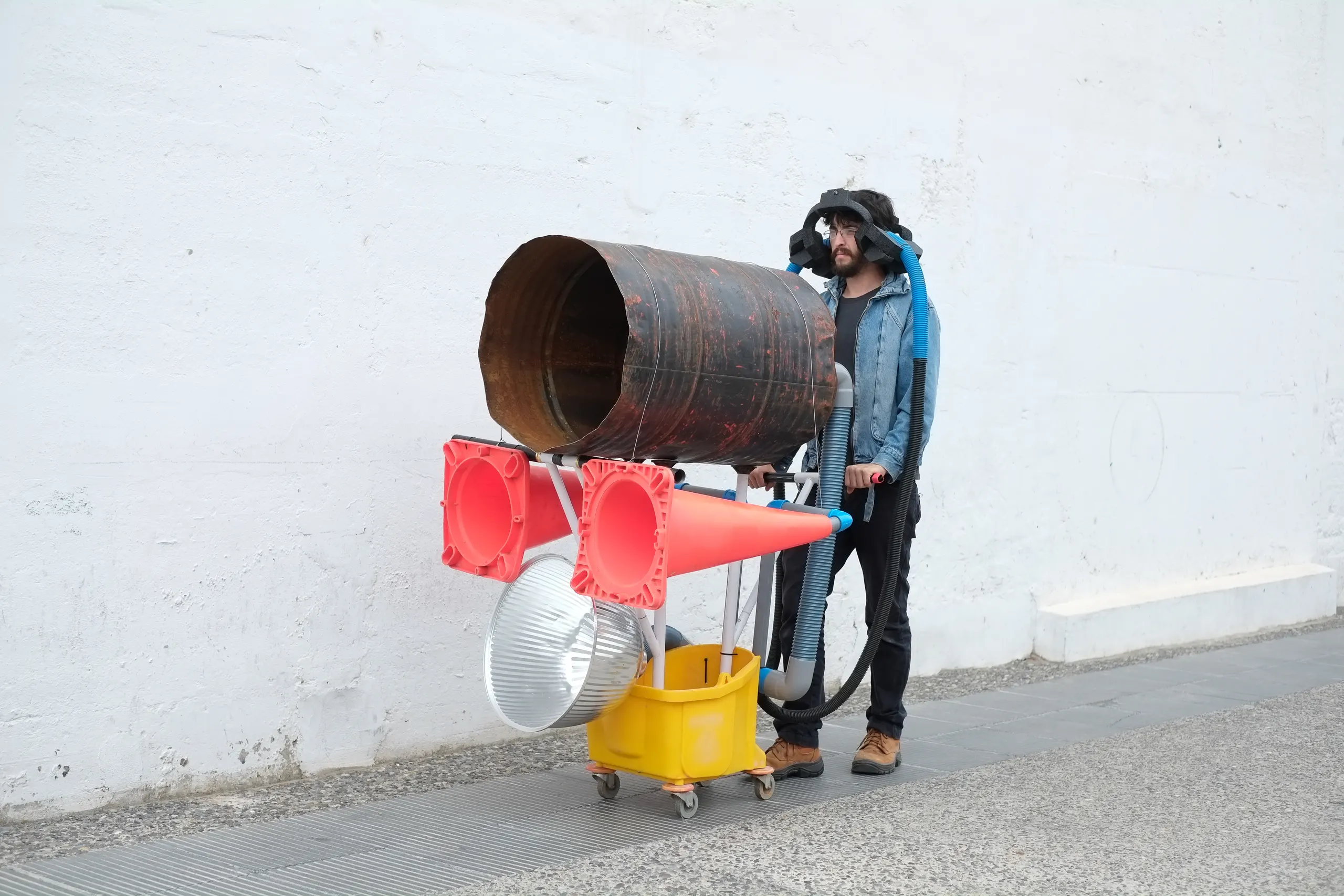 Photo of a man pushing a cart made out of resonant items like drums and tubes.