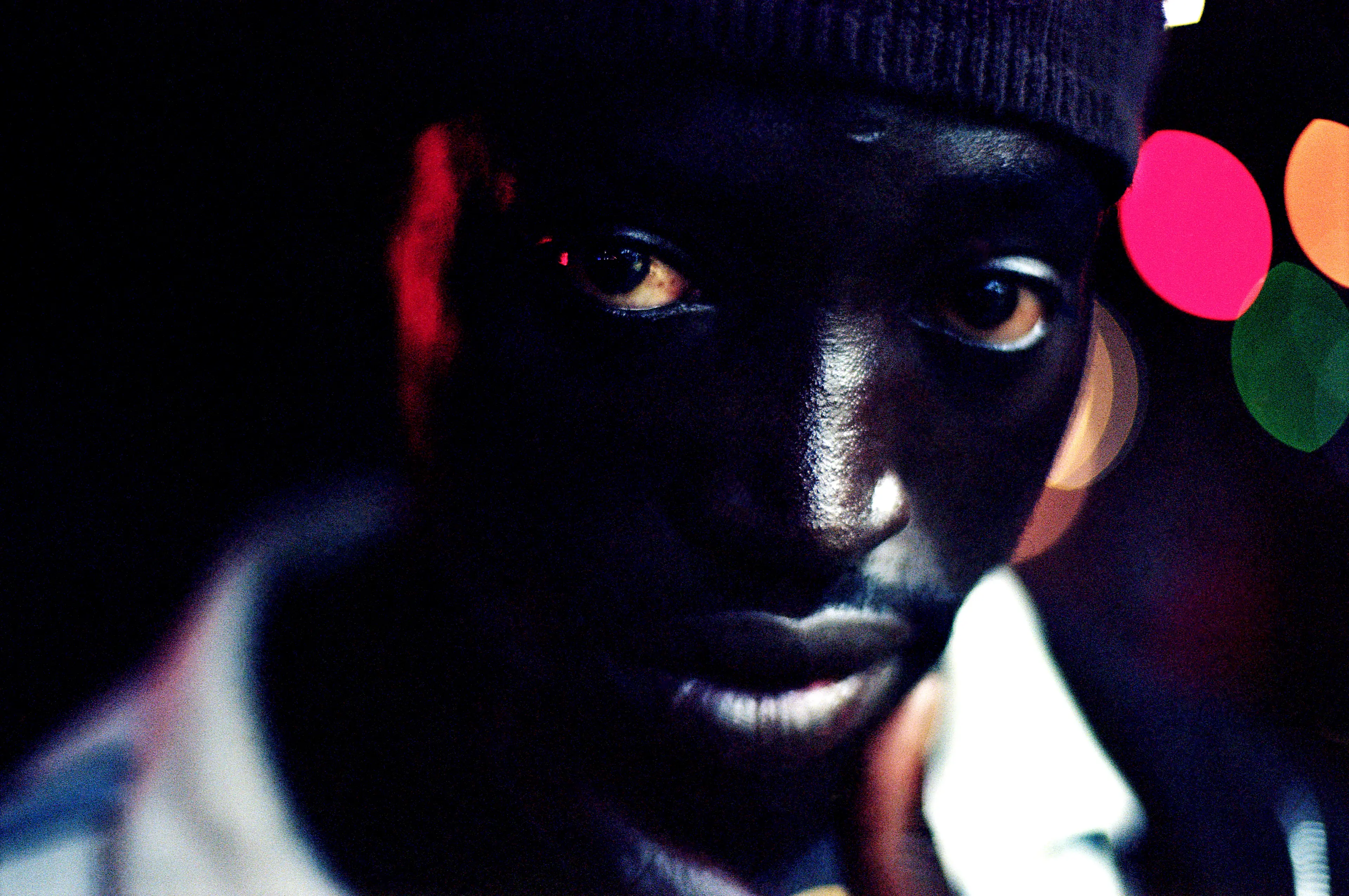 Close up photo of black man in dark surroundings, looking straight at the camera, where only eyes and a few facial features are visible.