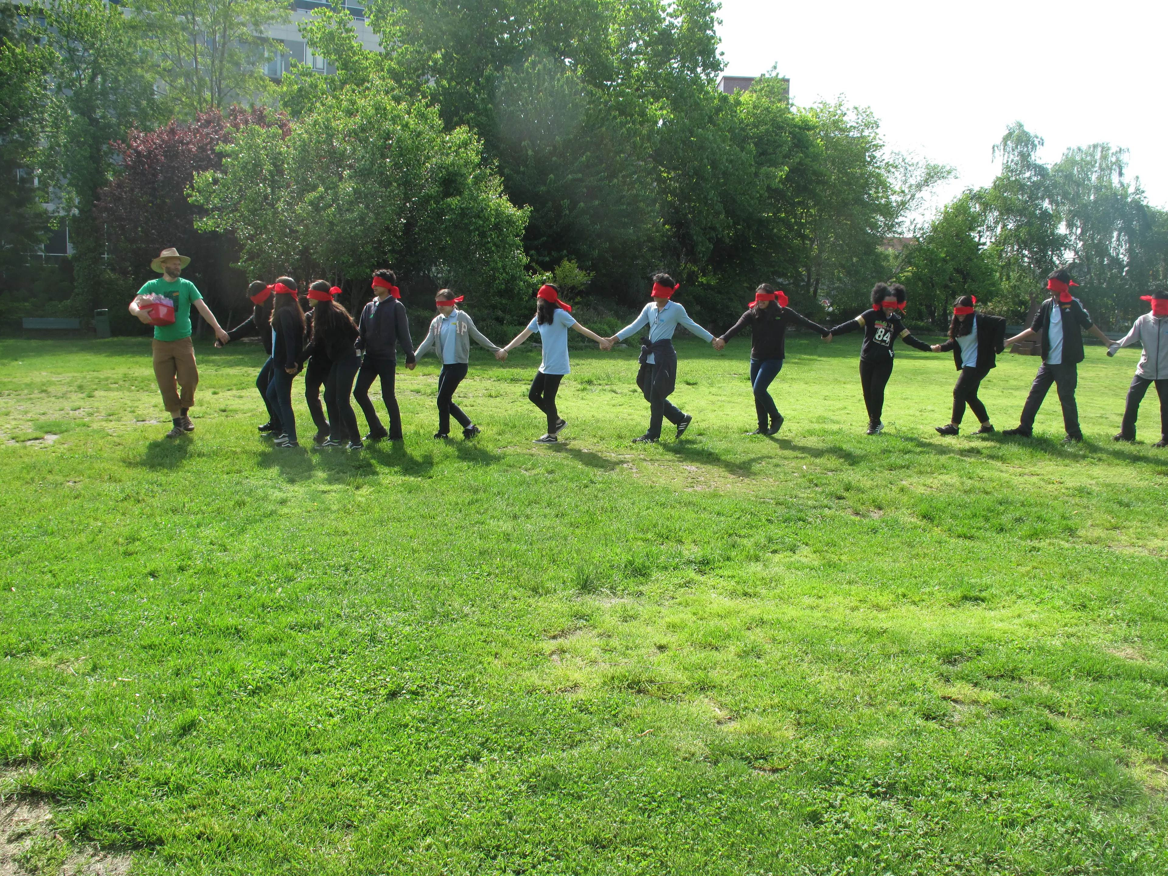 Photo of 12 kids holding hands and walkgin in a park wearing red headbands and being led by Doug.