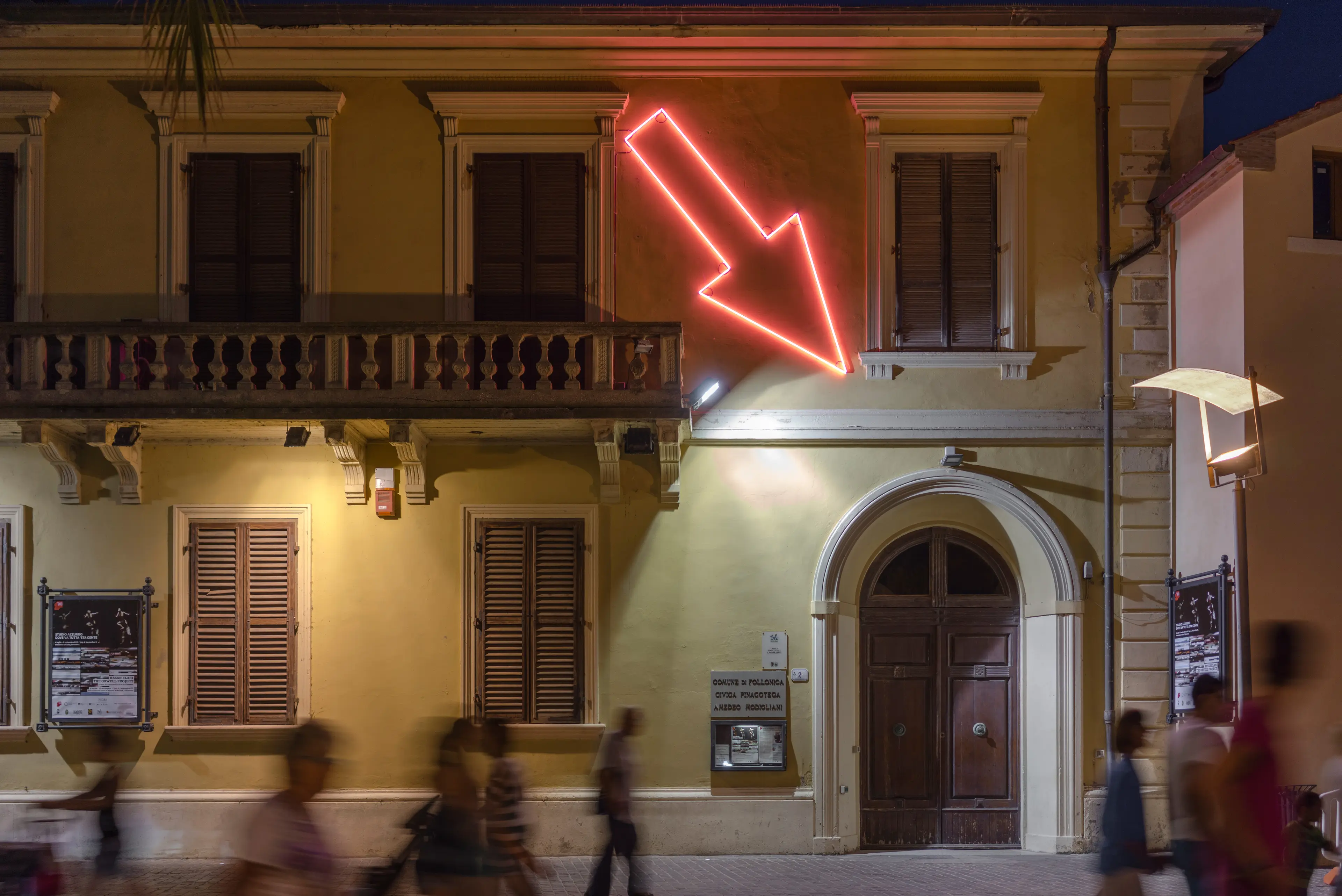 Picture of large red neon arrow pointing down to the right towards a door.
