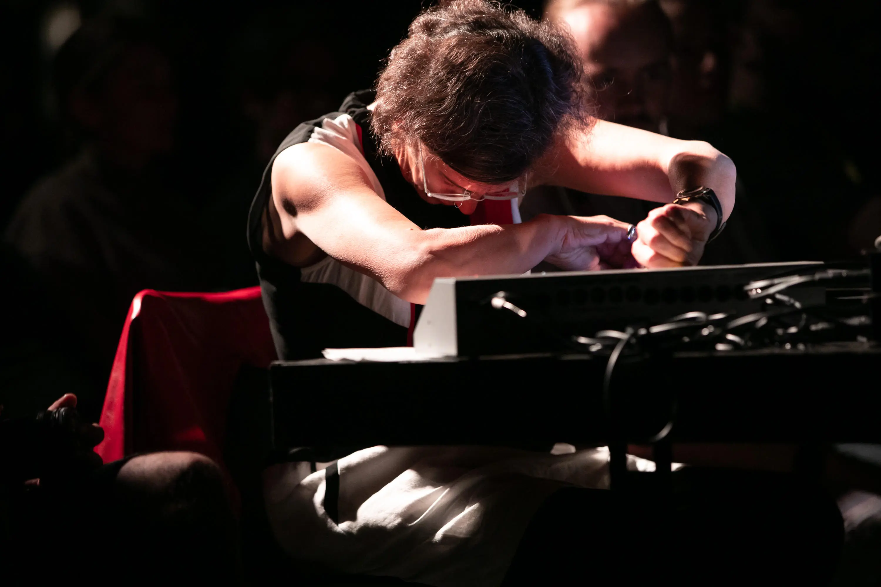 Photo of Schimana, face down, with hands crossed over a mixing console, looking concentrated.