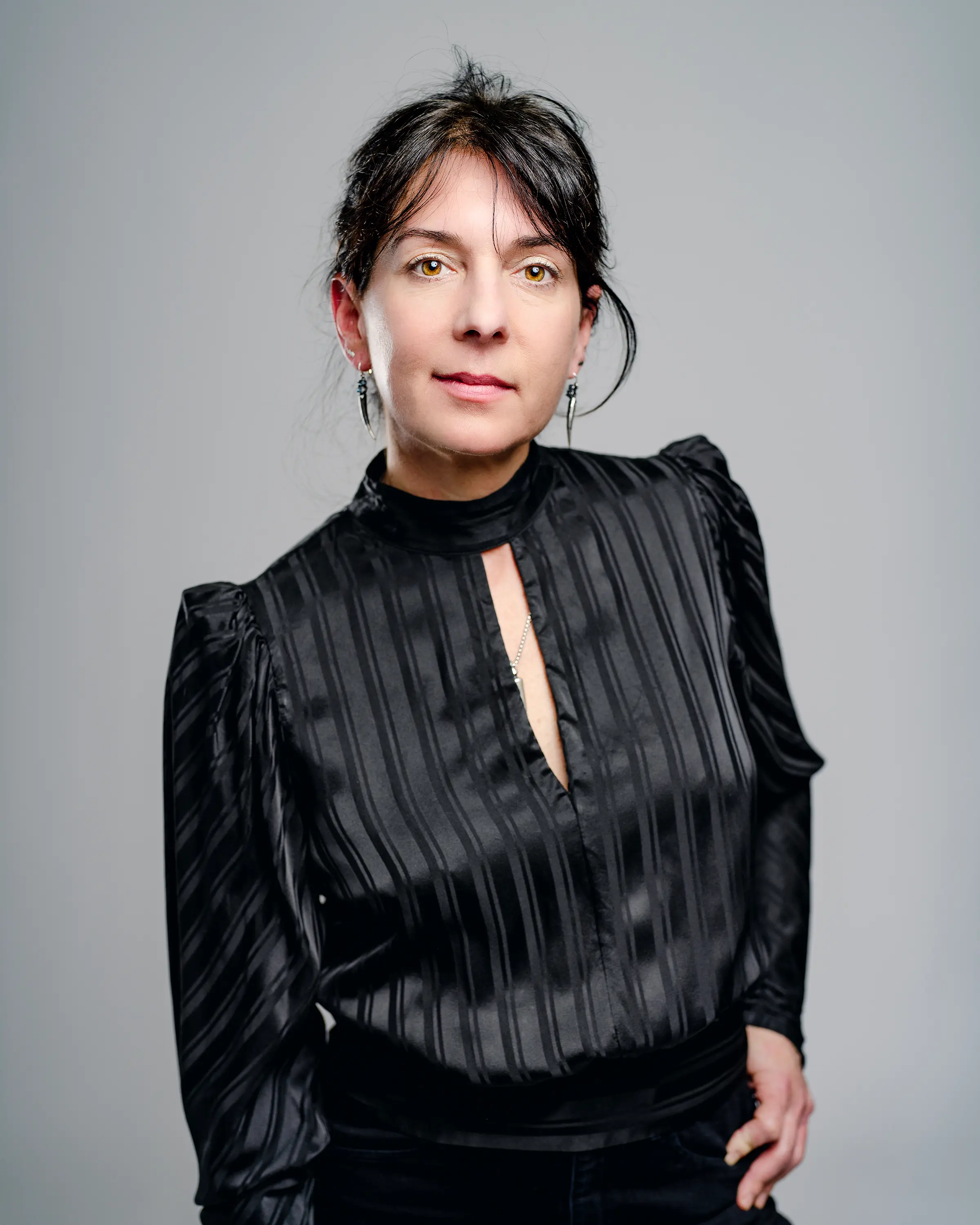 Photo portrait of Galen, a white woman with dark hair and eyes, in an elegant black dress with puffed shoulders.  She is looking straight at the camera with a soft smile and dangling earrings.