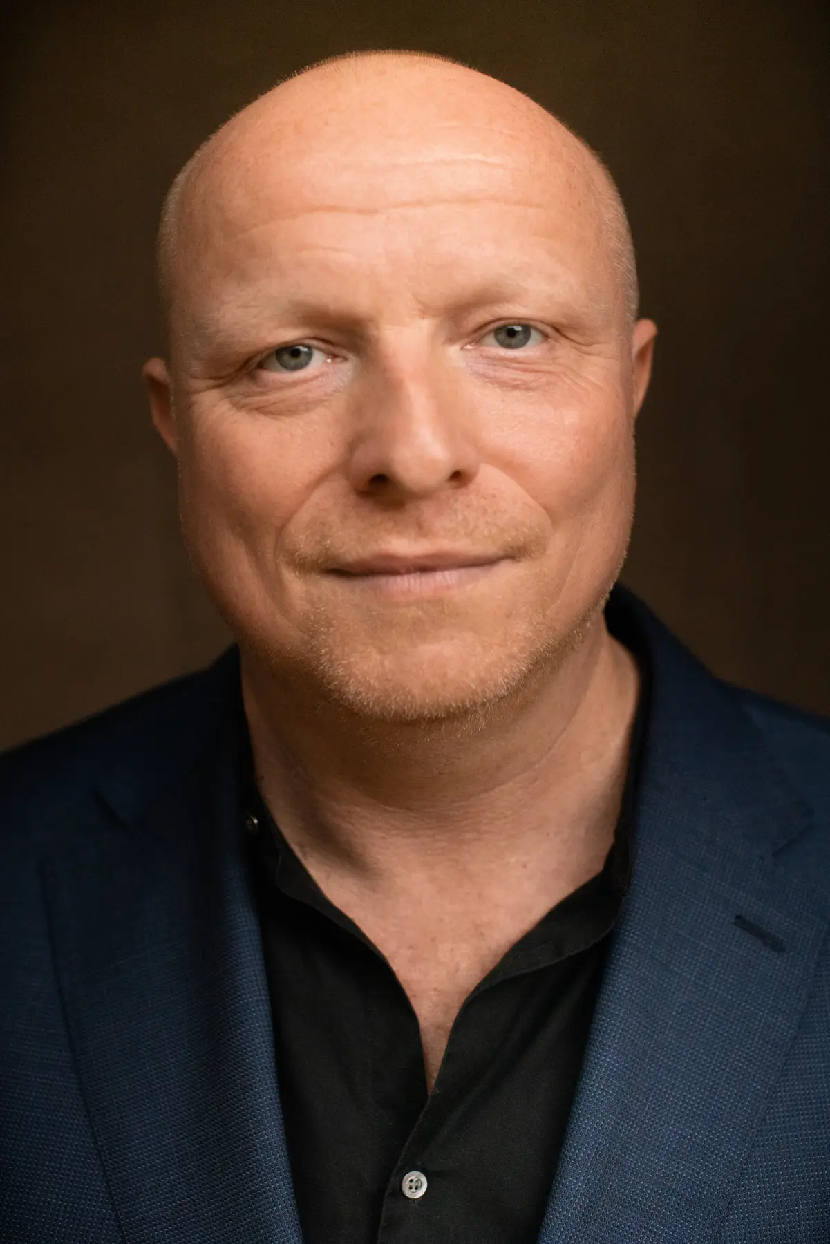 Photo portrait of Holger Schulze from the front looking straight into the camera with a black shirt and blue blazer.