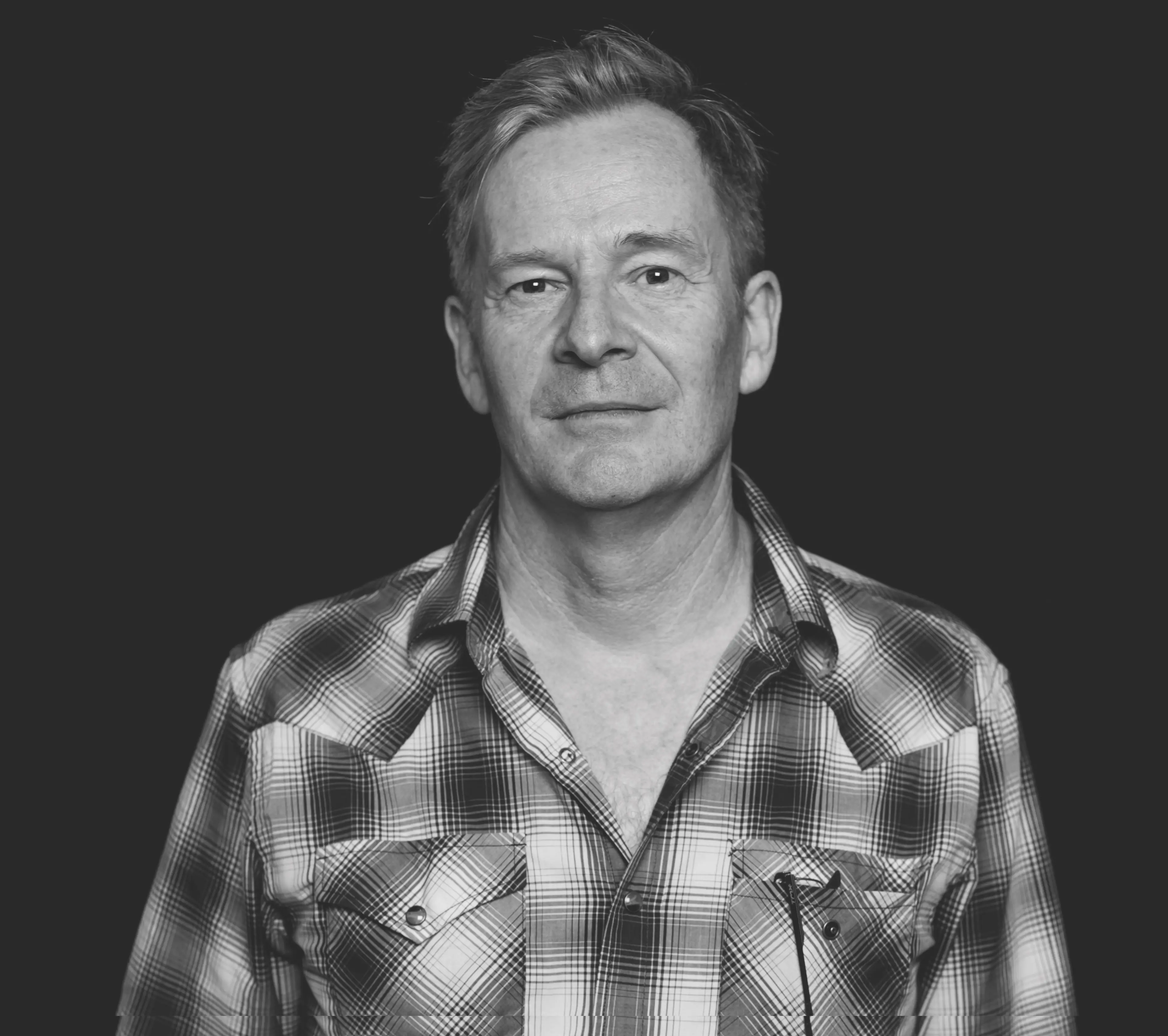 Black and white photo of white man facing camera with plaid shirt