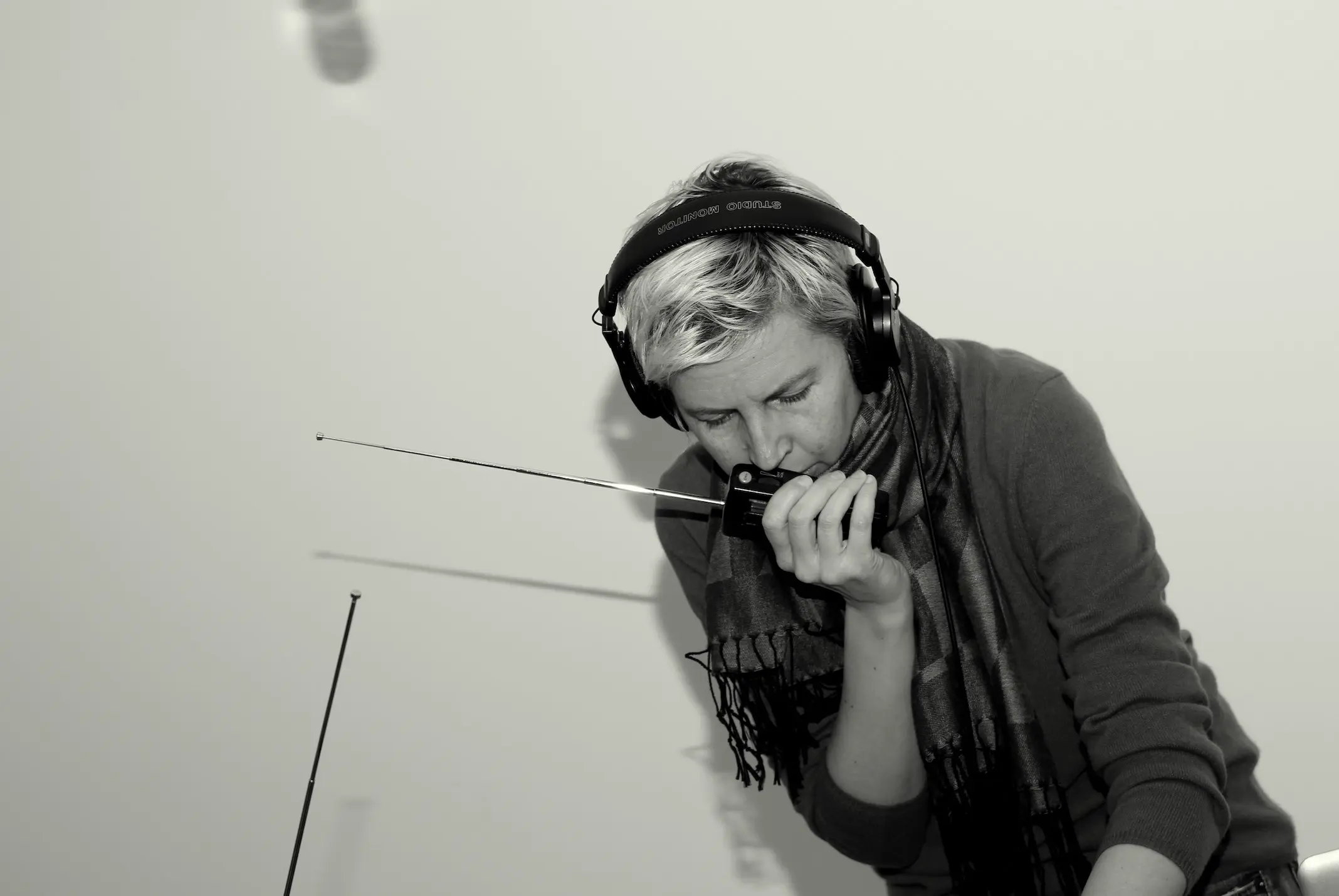 Photo of Anna Friz in headphones and speaking into walkie talkie with a long antenna